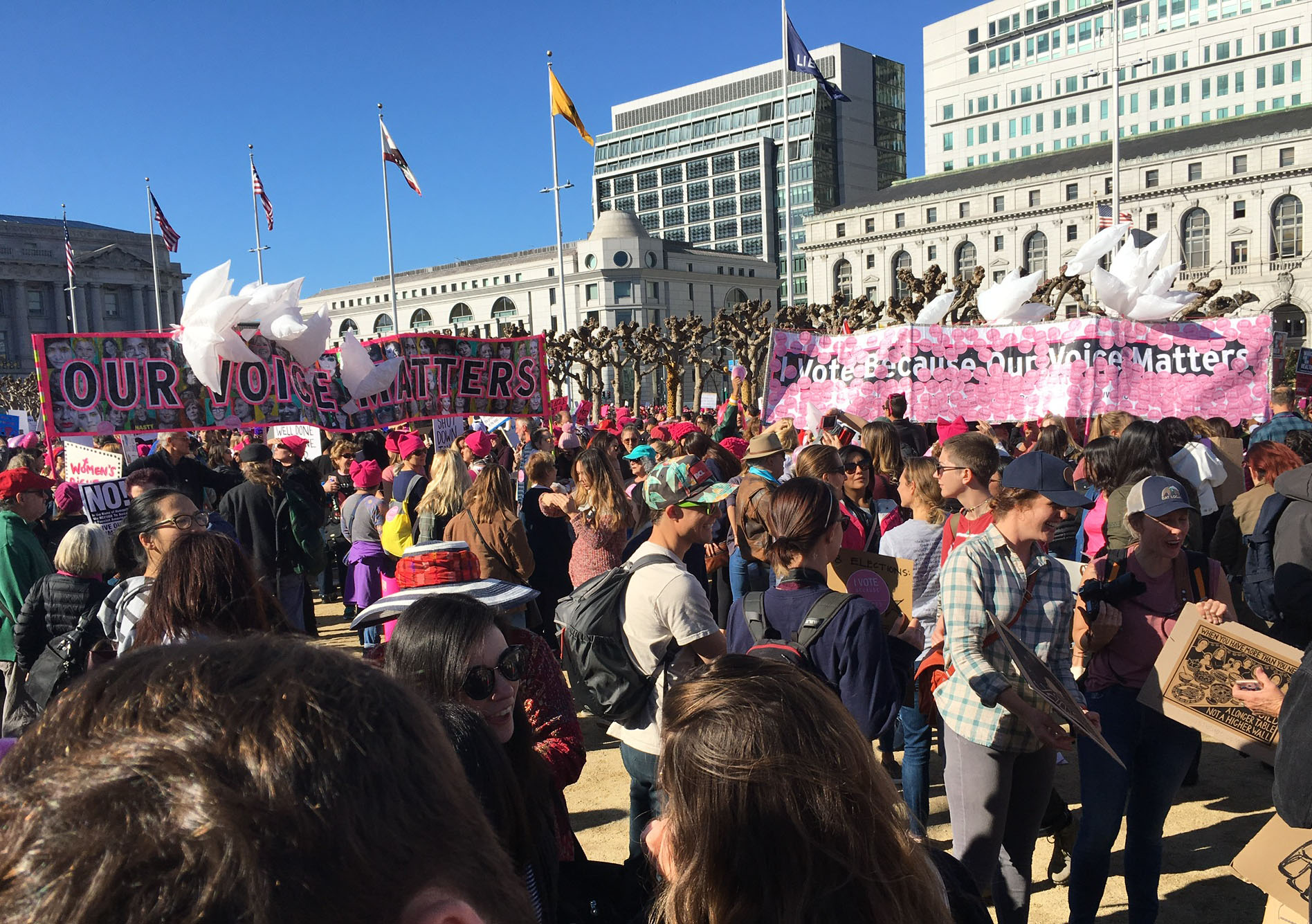 Two banners are held above a crowd of marchers in Civic Center Plaza