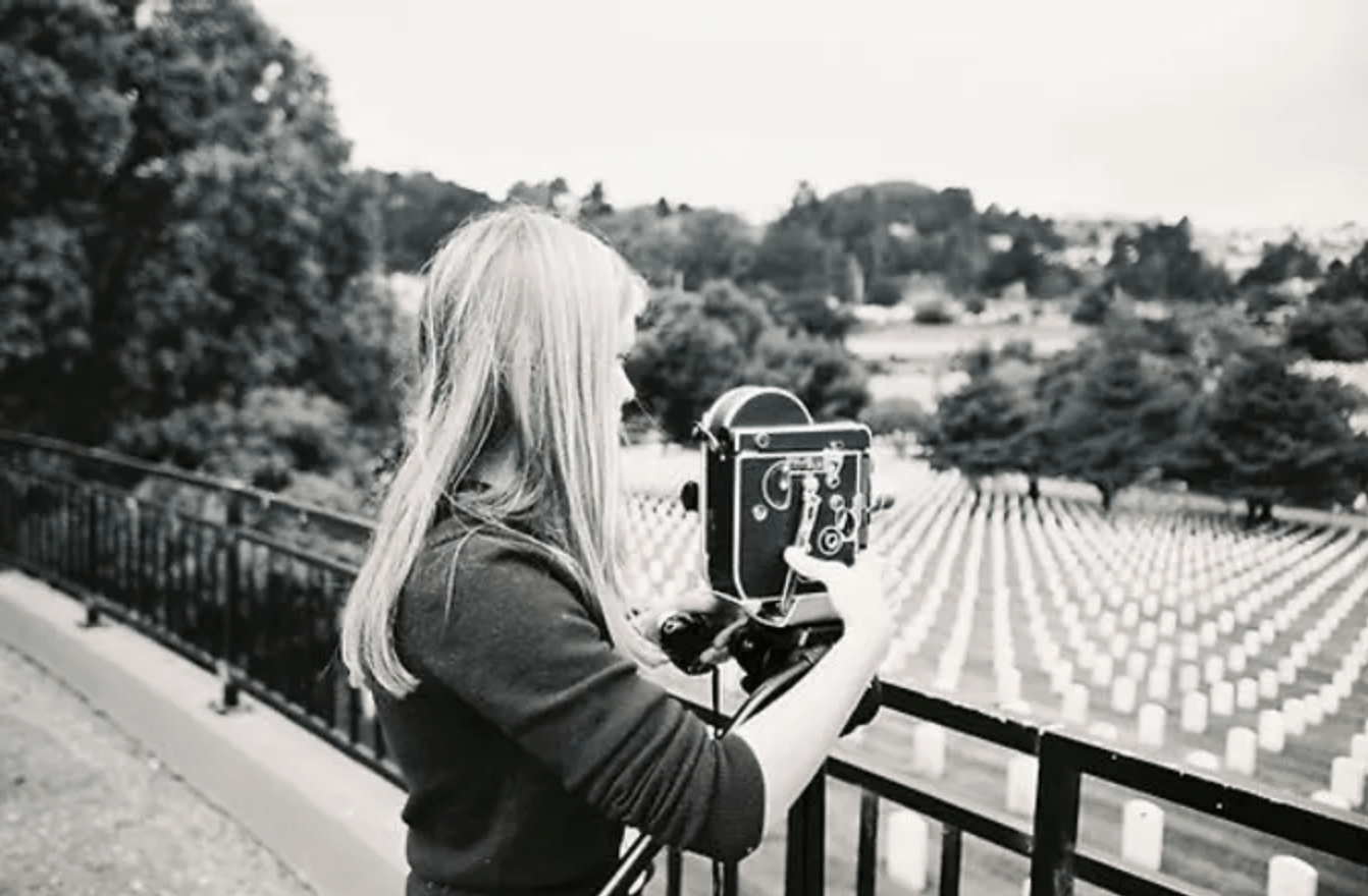 a young woman holding an antique movie camera filming a cemetary