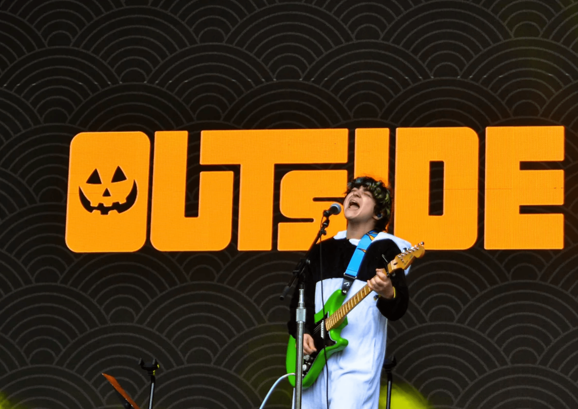 a singer holding a guitar in front of a large sign that says outside