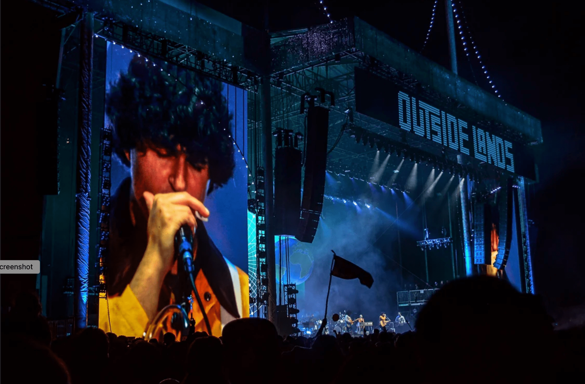 a close up of a singer on a video screen next to a large outdoor stage