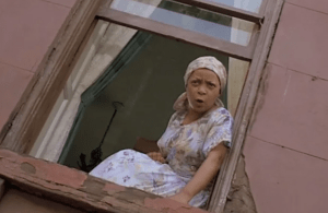 an older black woman sits in her window talking to someone on the street below