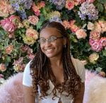 a young woman with braids and glasses sitting on a furry chair against a flowery background