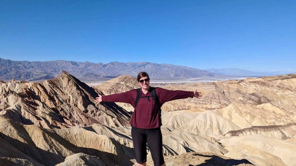 woman holding out her arms against a panoramic view of Death Valley desert
