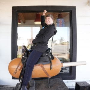 young woman riding a coin op horsey machine shaped like a corn dog