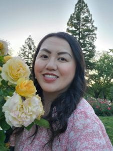 Sheng poses for a headshot with flowers in a garden.