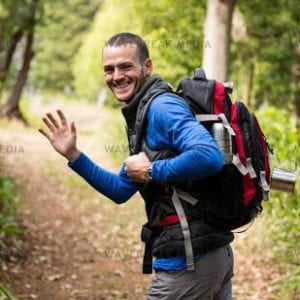 Portrait of male hiker waving hand while walking in forest