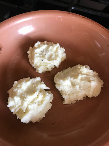 Three dollops of mashed potatoes in a frying pan.
