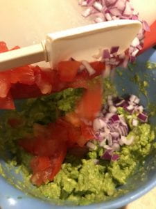 Adding the other ingredients to the mashed guacamole in a bowl.