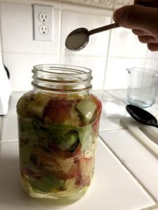 Pouring a spoonful of a sugar with a jar of water and apple scraps.