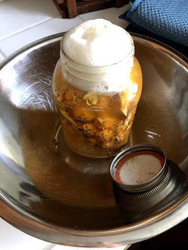 An opened jar of pineapple water overflowing with white foam.