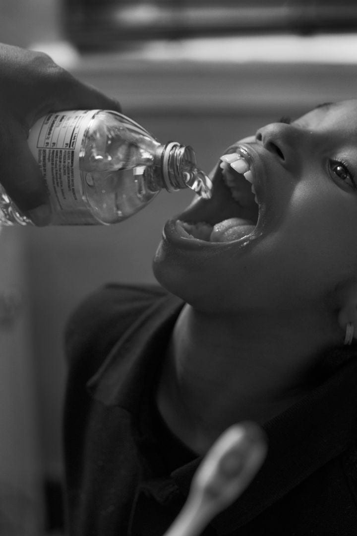 Child having water poured into their mouth from a plastic bottle.