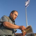 A man reading from a parayer book beneath the Israeli flag.