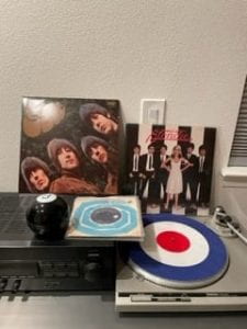 A record turntable with vinyl album covers placed behind it.